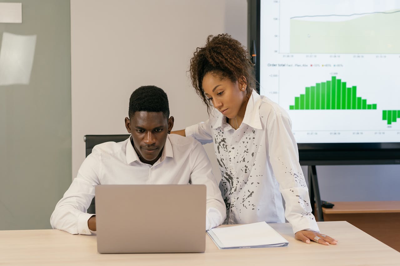 Two professionals collaborating over a laptop with data charts in the background.