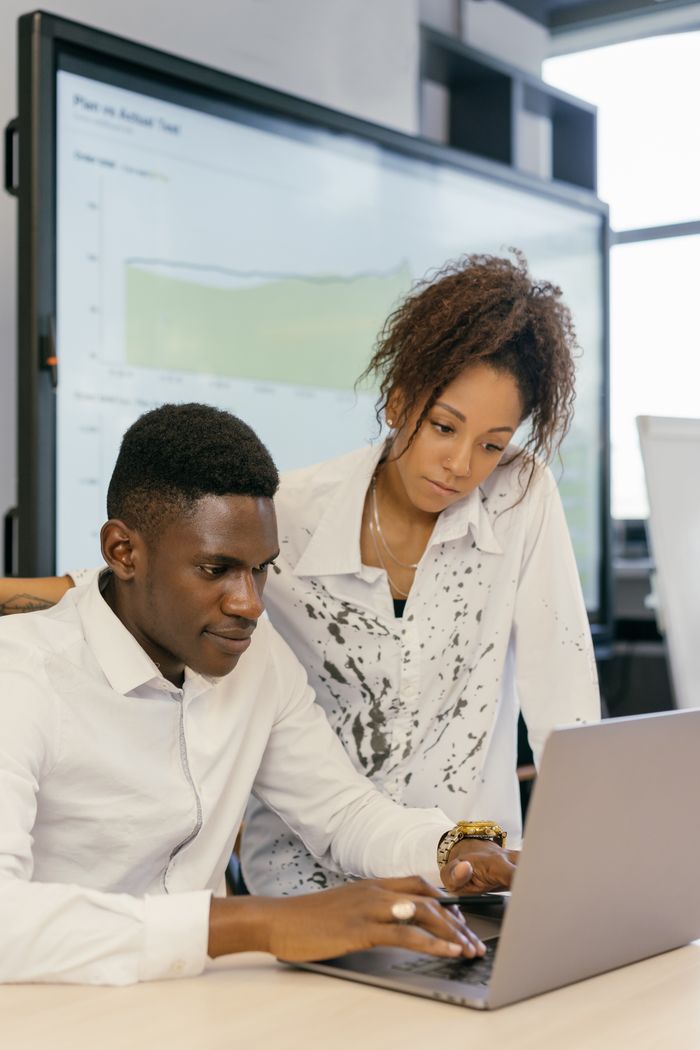 Two colleagues working together on a laptop in a modern office environment.
